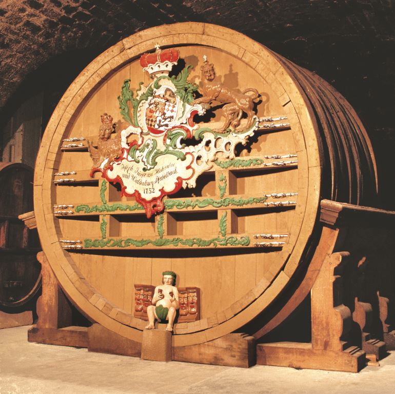 Ein sehr großes, liegendes Weinfass aus Holz mit hölzernem Schmuck an der Front ist zu sehen.