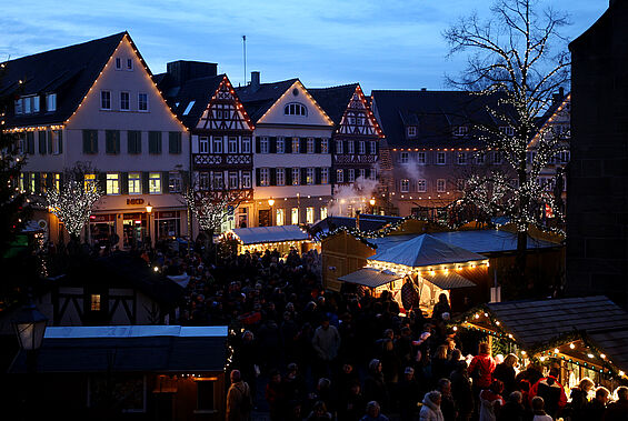 Ein Weihnachtsmarktbild von Öhringen ist zu sehen mit Menschen und Lichtern.