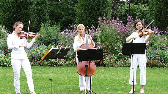 Drei Musikerinnen in weiß gekleidet sind zu sehen.