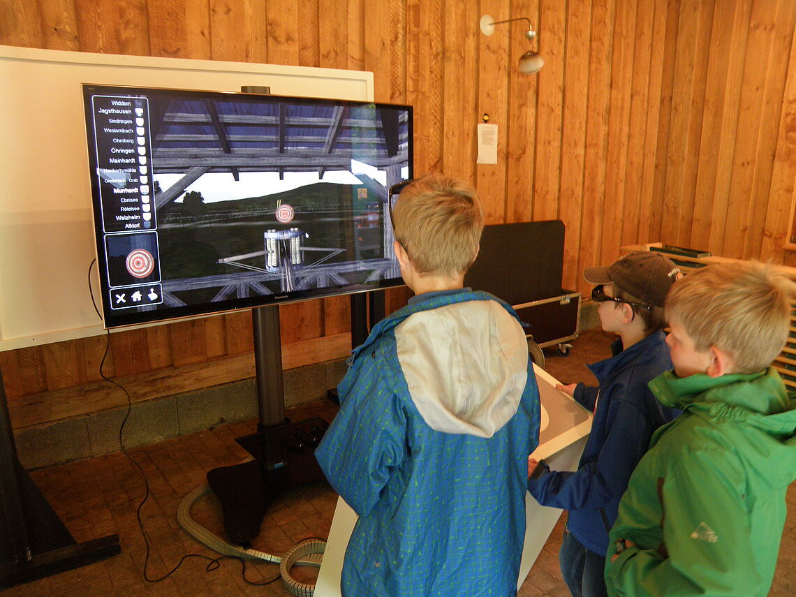 Drei Jungen stehen vor einem Bildschirm und nutzen die Virtuellen Limeswelten.