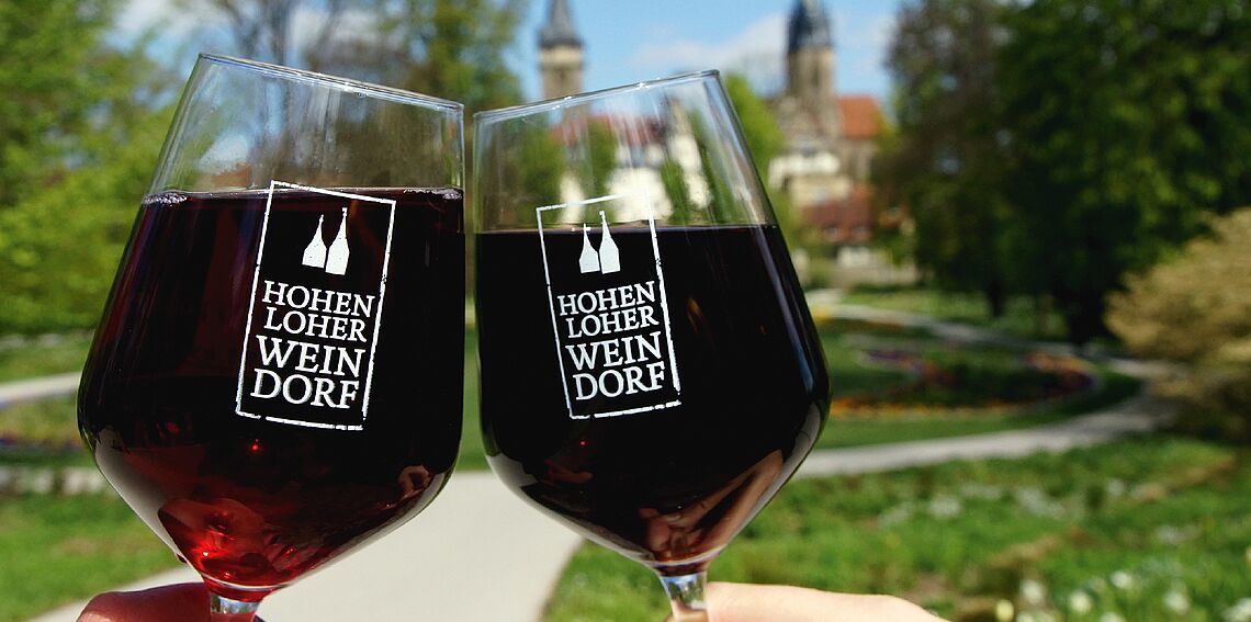 Zwei Rotweingläser mit dem Logo des Hohenloher Weindorfes sind zu sehen.