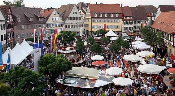 Ein Luftbild vom Öhringer Weindorf ist zu sehen mit den Häusern rund um den Marktplatz, Menschen und großen Schirmen.