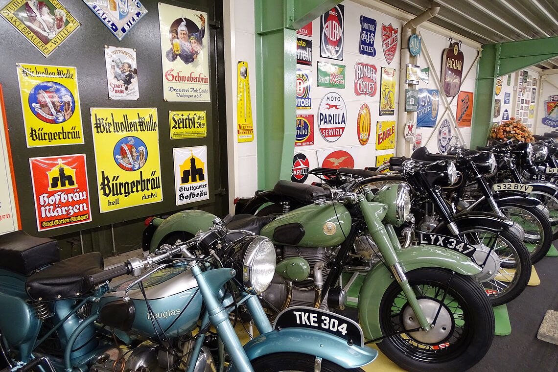 Im Vordergrund Oldtimer-Motorräder, im Hintergrund Emaille-Schildern, alles im Motor Museum Öhringen.