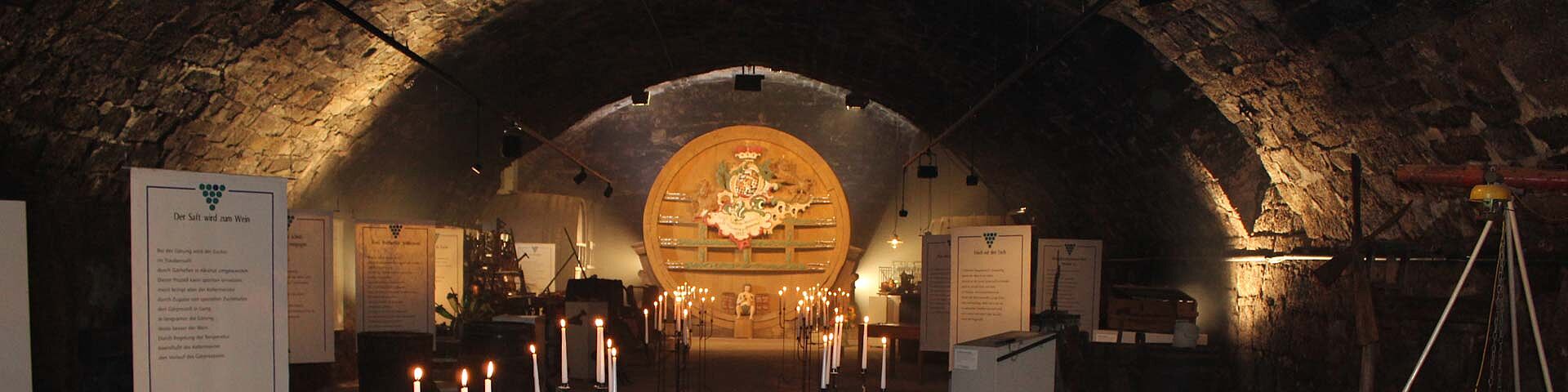 Das in Kerzenschein getauchte Weinbaumuseum mit großem Faß im Hintergrund ist zu sehen.