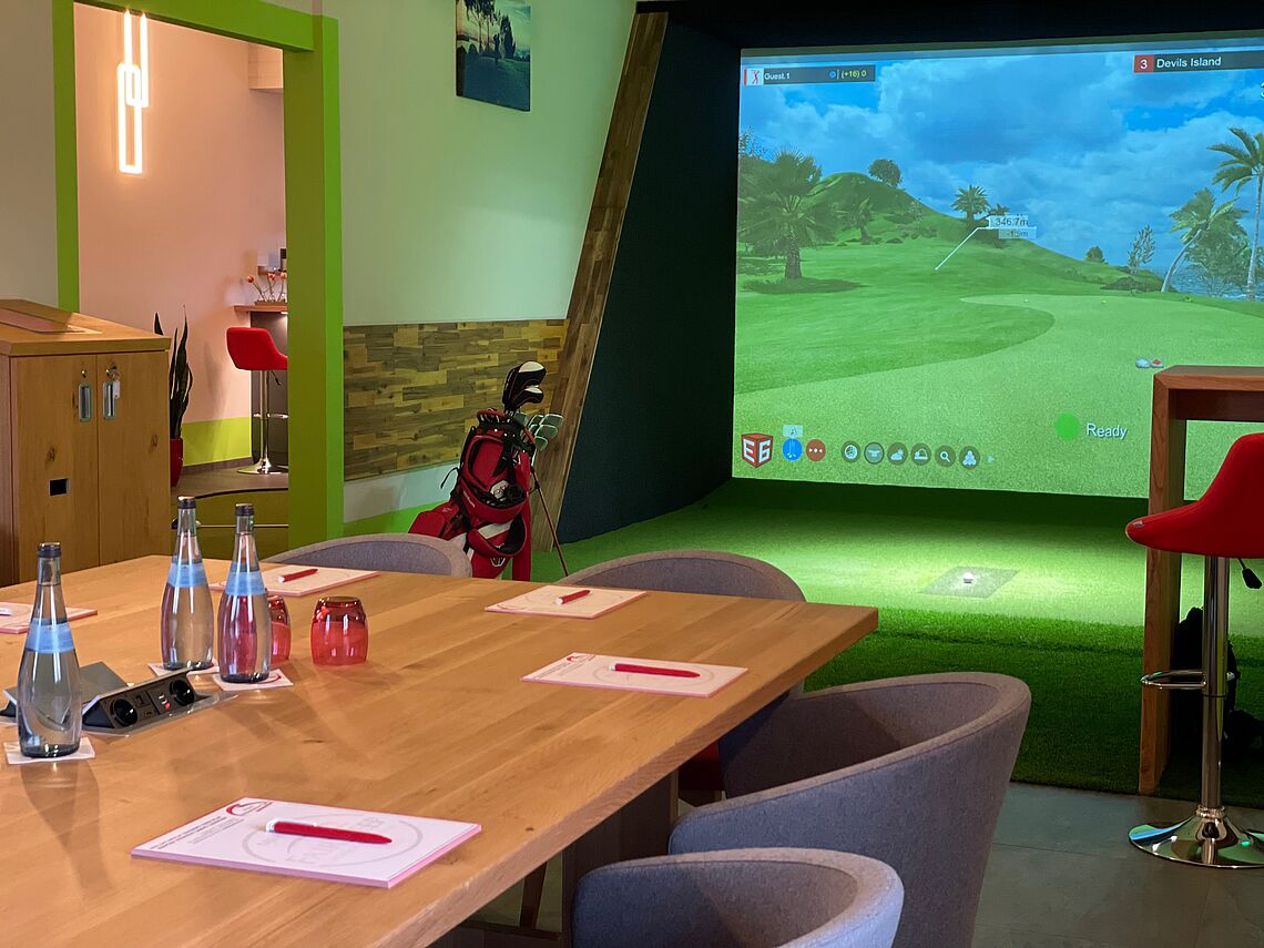 Tisch im Vordergrund, Bildschirm für Indoor Golf im Hintergrund