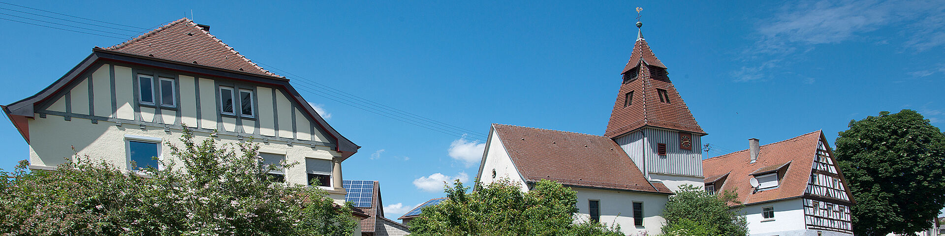 Fachwerkhäuser und eine kleine Kirche in Zweiflingen sind vor blauem Himmel zu sehen.