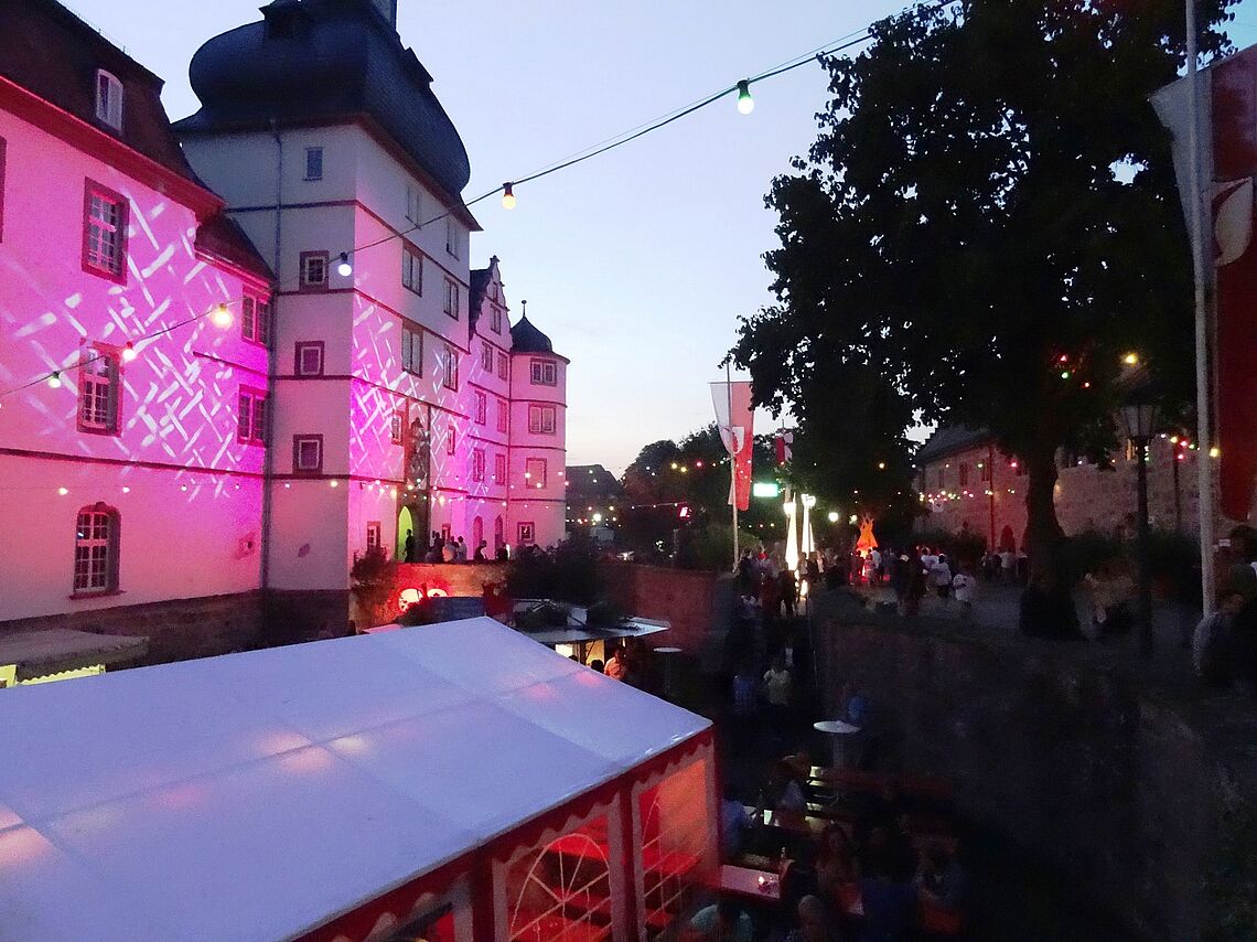 Das Pfedelbacher Schlossfest ist zu sehen. Links ist das Schloss rosa beleuchtet.