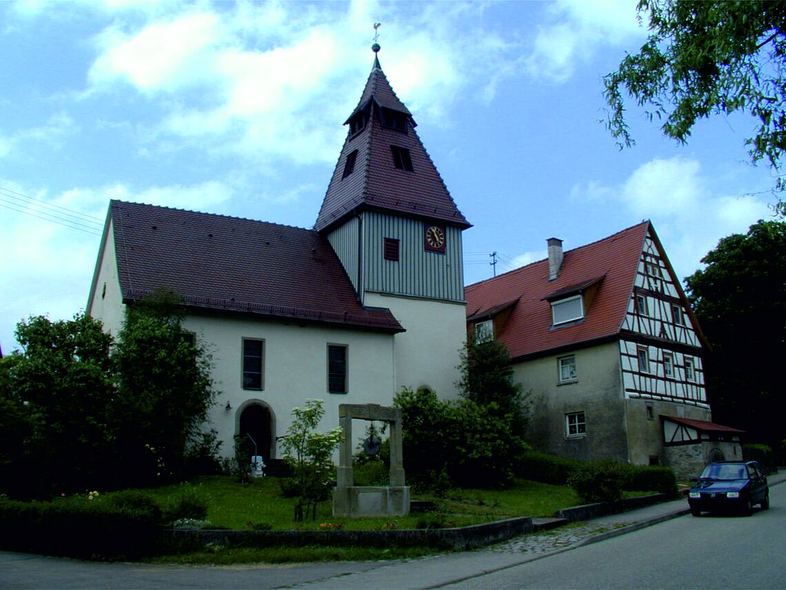 Links ist die St. Nikolaus Kirche in Zweiflingen zu sehen, rechts ein Fachwerkhaus sowie ein Pkw.