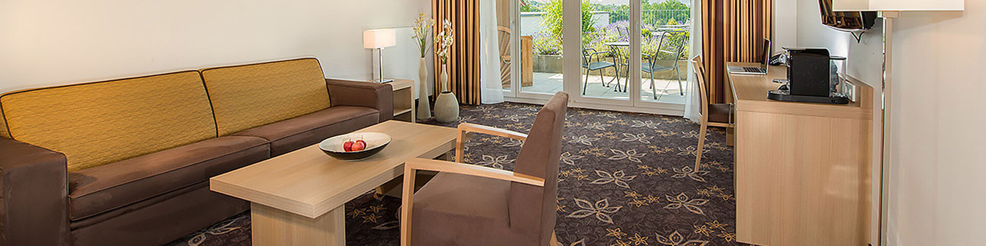 Ein Hotelzimmer mit Sofa, Tisch, Sessel und Schränkchen ist zu sehen.