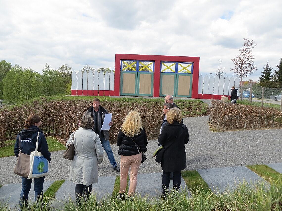 Eine Gruppe lauscht dem Vortrag eines Führers. Im Hintergrund ist das farbige Limes Tor in Öhringen zu sehen.