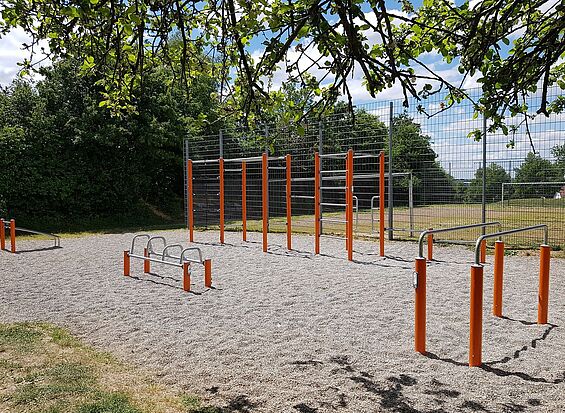 ein oranger Fitnessparcours ist zu sehen, im Vordergrund die Äste eines Baumes.